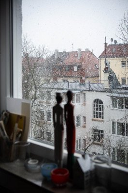statuettes on windowsill looking outside, snow on houses 