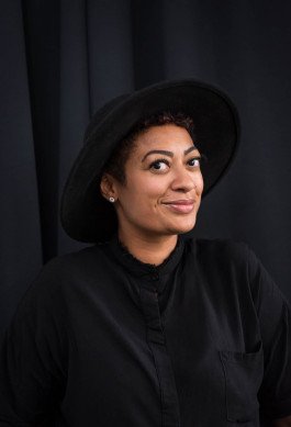 portrait of woman with black clothes and hat in front of black background 